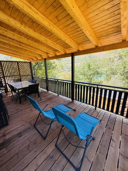 Terrasse en bois avec chaises bleues dominant le lac et les montagnes aux Cabanes du Belvédère, Serrières-sur-Ain
