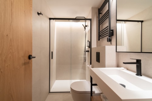 Baño moderno del Hotel Bruna con cabina de ducha de marco negro, tocador blanco y toallero calefactor