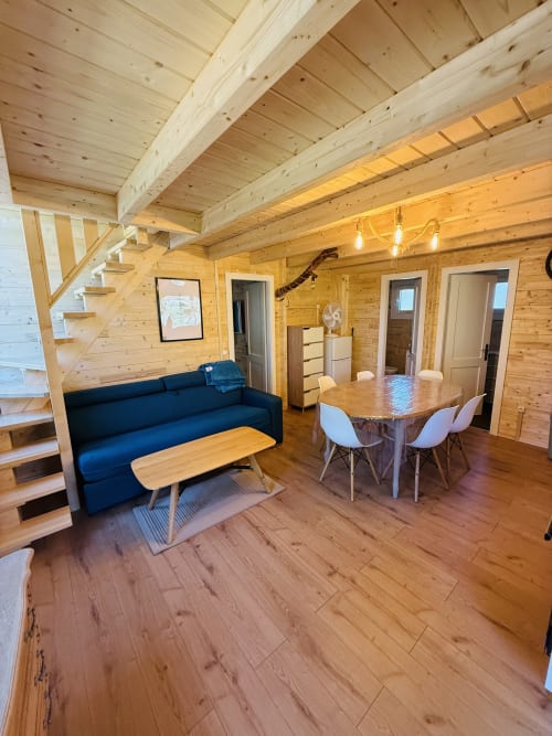 Intérieur chaleureux de chalet en bois avec canapé bleu, table à manger et plafond aux poutres apparentes aux Cabanes et lodges du Belvédère