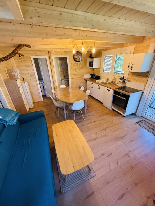 Intérieur de lodge moderne avec poutres en bois, cuisine équipée, table à manger, canapé bleu et lumière naturelle