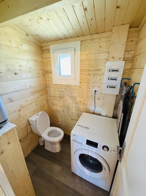 Salle de bain moderne dans un lodge en bois avec toilettes, lave-linge et tableaux électriques aux Cabanes du Belvédère