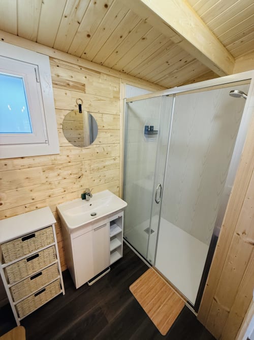 Salle de bains moderne de la villa Lodge le Quercus avec murs en bois, vasque blanche, douche vitrée et carrelage foncé