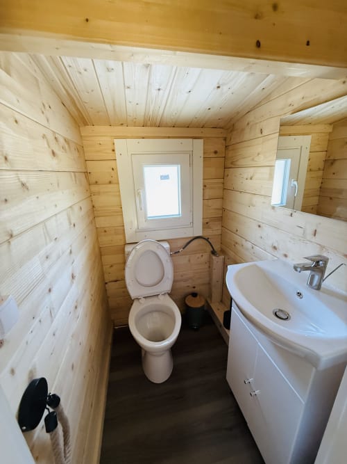 Salle de bain moderne dans un lodge en bois avec toilettes, lavabo, miroir et fenêtre aux Cabanes et lodges du Belvédère