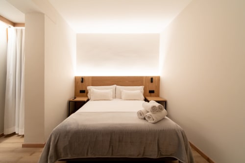 Moderna habitación doble en Hotel Bruna con cabecero de madera, ropa de cama color crema e iluminación ambiental