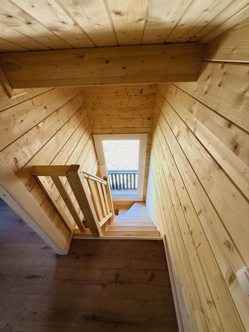 Escalier en bois du lodge avec rampe menant à l'étage supérieur et terrasse vue sur le lac, Cabanes et lodges du Belvédère
