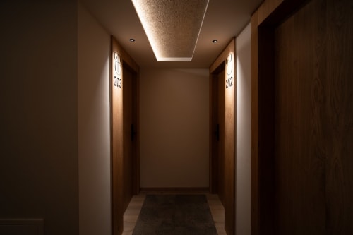 Pasillo moderno del Hotel Bruna con puertas de madera, iluminación ambiental en techo y apliques contemporáneos en Esterri