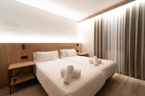 Habitación moderna del Hotel Bruna en Esterri D'Àneu con camas gemelas, cabecero de madera y cortinas de piso a techo.