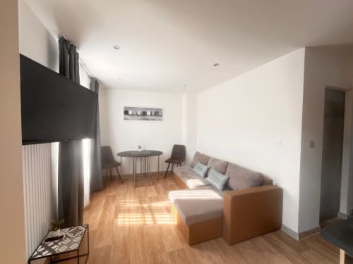 Séjour moderne avec téléviseur écran plat, canapé sectionnel beige, table ronde et parquets à La Villa L'Oiseau