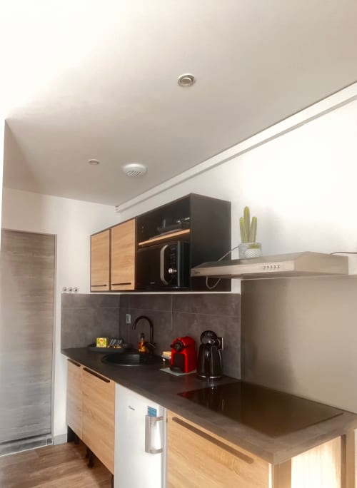 Kitchenette moderne dans l'appartement 1 chambre de La Villa L'Oiseau Bleu, Blonville-sur-Mer avec comptoirs noirs et armoires en bois