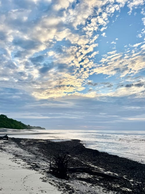 Dramatic coastal dawn at El Litoral Wellness Retreat with rocky beach, gentle waves, and blue sky