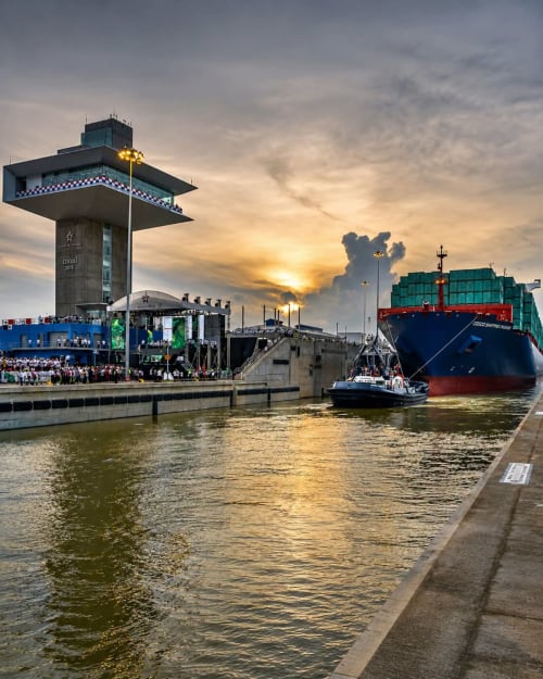 Large cargo ship docked at industrial port at sunset with control tower and crowds