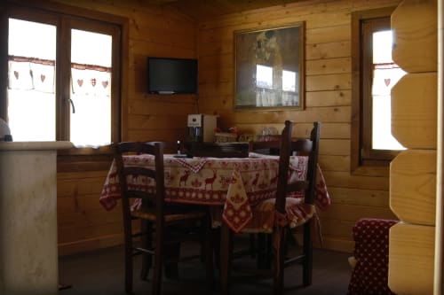Accogliente zona pranzo dell'appartamento Casa Civetta con pareti in legno rustico, tovaglia rossa festiva e TV in Country House Bosco