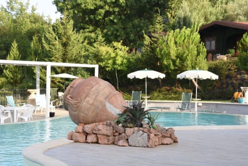 Pool area at Country House Bosco d'Olmi with decorative stone sphere, umbrellas, and surrounding trees in Sant'Andrea del