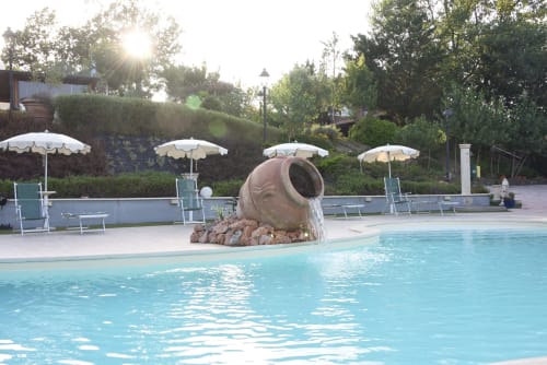 Resort pool at Country House Bosco d'Olmi with decorative water feature, sun umbrellas, and lounge chairs