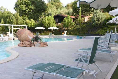 Bosco d'Olmi pool area with loungers, umbrellas, and decorative stone sphere in Sant'Andrea del Garigliano