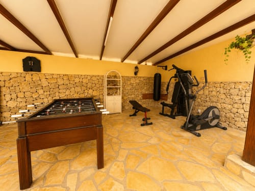 Game room in Casa Emilia villa with foosball table, stationary bike, and exercise equipment on stone flooring