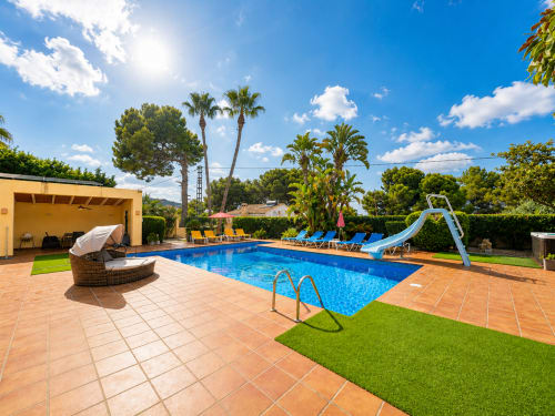 Casa Emilia villa in Moraira featuring a private pool, blue water slide, lounge chairs, and manicured garden under sunny