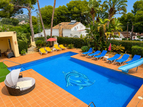 Sunny poolside at Casa Emilia villa in Moraira with blue loungers, terracotta patio, and Mediterranean landscape views