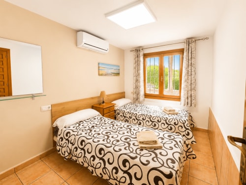 Bright twin bedroom in Casa Emilia villa, Moraira with wooden beds, patterned bedding, French doors opening to garden views,