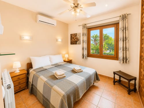 Bright bedroom in Casa Emilia villa, Moraira with queen bed, wood nightstands, garden views through double doors, and