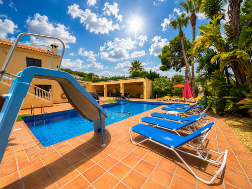 Casa Emilia villa pool in Moraira with blue slide, loungers, terrace and palm trees under sunny sky