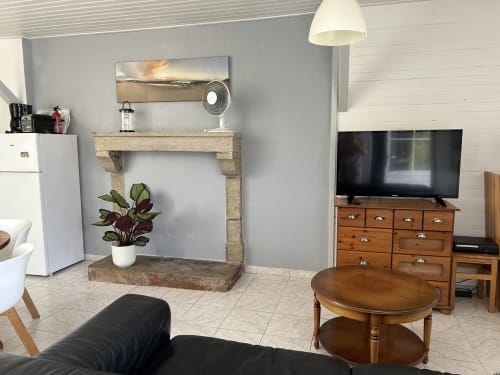 Gîte Les Plages living room with stone fireplace, TV on wooden dresser, round coffee table, and modern amenities at Le Pré