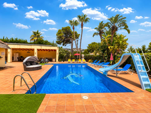 Casa Emilia villa pool in Moraira with blue water, loungers, slide, palm trees and terracotta patio