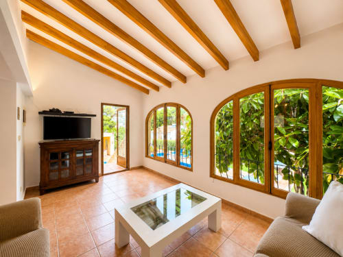 Bright living room in Casa Emilia villa, Moraira with wooden beams, terracotta floors, TV, and pool views through arched