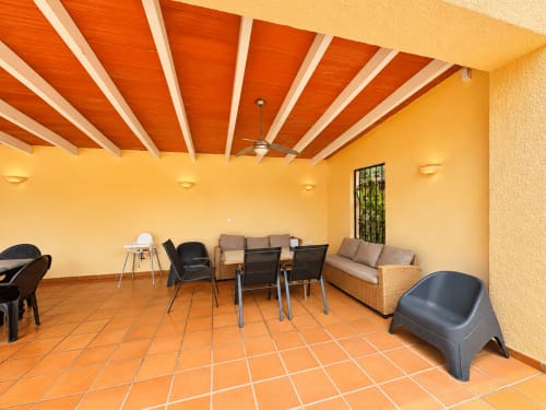 Spacious covered terrace at Casa Emilia villa in Moraira with orange tile floor, yellow walls, and orange beamed ceiling