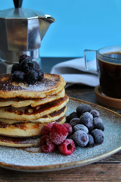 Stack of fluffy pancakes dusted with powdered sugar, topped with berries, served with coffee at Country House Bosco d'Olmi