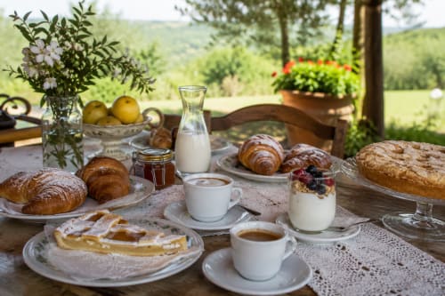 Outdoor breakfast spread at Bosco d'Olmi countryside B&B with pastries, coffee, yogurt, and Italian countryside views.