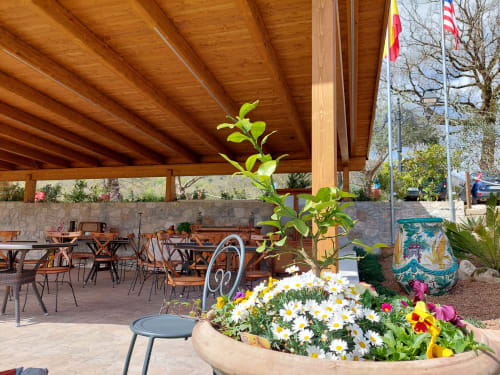 Covered patio dining area at Country House Bosco d'Olmi with wooden beams, colorful flower beds, and Italian flags