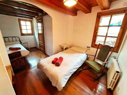 Habitación espaciosa en L'Orri Rectoria Nova B&B de Campelles, Girona, con vigas de madera, camas gemelas y grandes ventanales.
