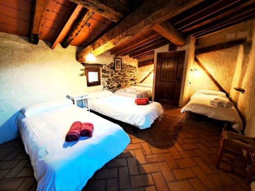 Dormitorio rústico en L'Orri Rectoria Nova de Campelles con vigas de madera, muros de piedra y varias camas con sábanas blancas