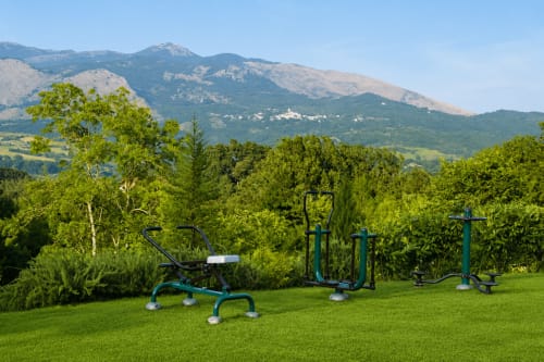Outdoor fitness equipment on green lawn at Bosco d'Olmi with mountains and forest backdrop in Sant'Andrea del Garigliano