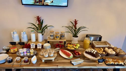 Mostrador de desayuno buffet de Casa Regina Tenerife con frutas frescas, pastelería, panes, mermeladas, zumos y plantas sobre mesa de madera