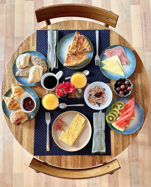 Desayuno completo en Casa Regina Tenerife: pasteles, tortillas, quesos, jamón, frutas y zumo servidos en mesa redonda de madera.
