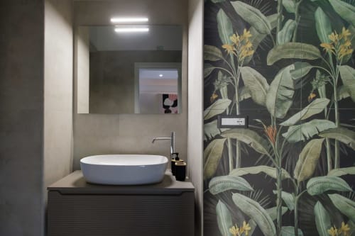 Bagno moderno della BellDuomo Suite Messina con lavabo rotondo bianco, specchio illuminato e carta da parati tropicale