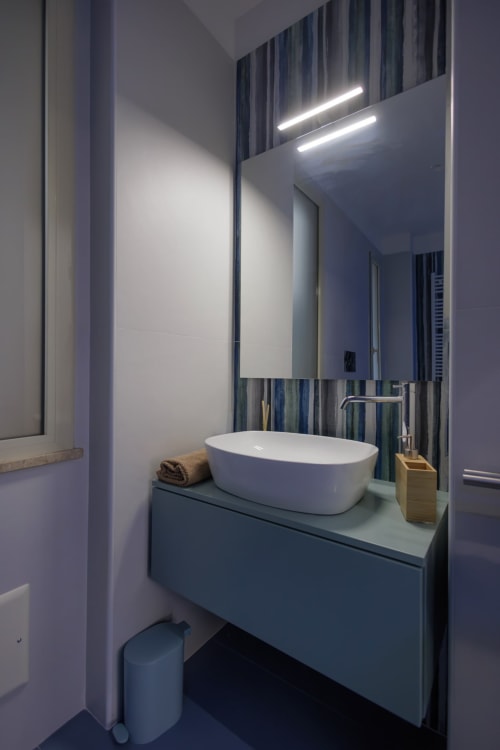 Bagno moderno della BellDuomo Suite Messina con lavabo bianco, specchio illuminato, carta da parati a righe e stile minimalista
