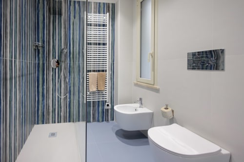 Bagno moderno nella BellDuomo Suite Messina con doccia walk-in, wc bianco, lavabo circolare e piastrelle blu a righe