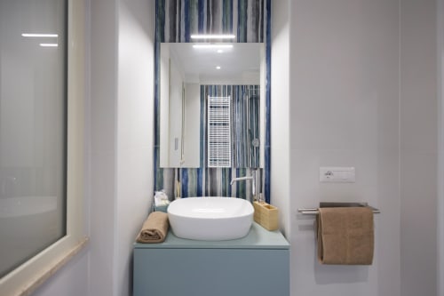 Moderno bagno della BellDuomo Suite Messina con lavabo bianco su vanità blu, tende righe blu e applique murale