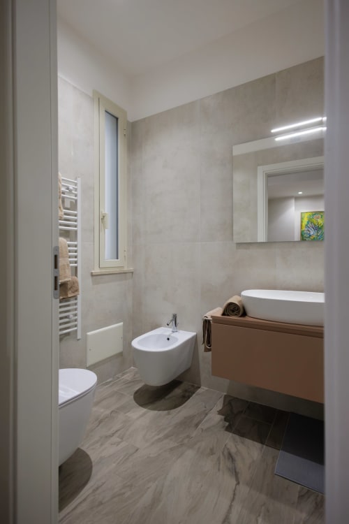 Bagno moderno della BellDuomo Suite Messina con sanitari bianchi, piastrelle beige e scaldasalviette