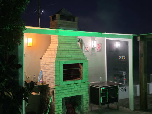 Área de churrasco em alvenaria verde vibrante na villa Philia em Florianópolis com cozinha externa e espaço de convivência, vista noturna