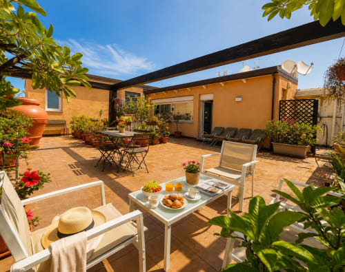 Soleggiata terrazza sul tetto del B&B Pellicano con villa arancione, vista mare, lettini, zona pranzo e fiori in vaso a Reggio