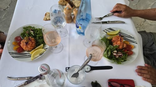 Repas en terrasse à House Carles à La Colle-sur-Loup : deux assiettes garnies de salade et crevettes, accompagnées de verres de rosé.
