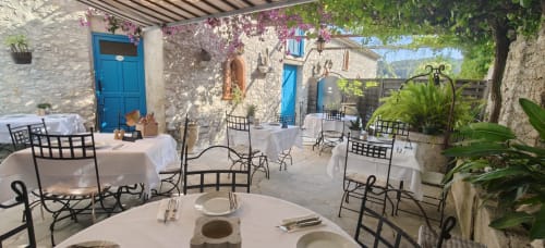 Cour de restaurant en plein air de la maison Carles avec murs en pierre, portes bleues et fleurs méditerranéennes à La Colle-sur-Loup