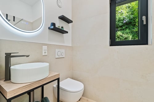 Salle de bain moderne du Mattbnb Ankoni Stay 3.2 à Metz avec vasque blanche, robinetterie noire, toilettes, miroir éclairé et