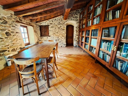 Rústica sala de biblioteca con vigas de madera, mesa de comedor y estanterías en la casa L'Orri Rectoria Nova de Campelles