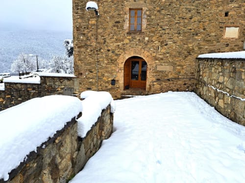 Casa de piedra cubierta de nieve L'Orri Rectoria Nova en Campelles con vistas montañosas y puerta de entrada de madera