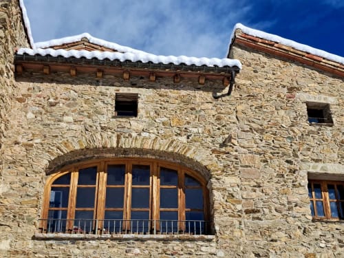 Casita de piedra en Campelles con ventana de arco de madera, tejado nevado y vistas a la montaña